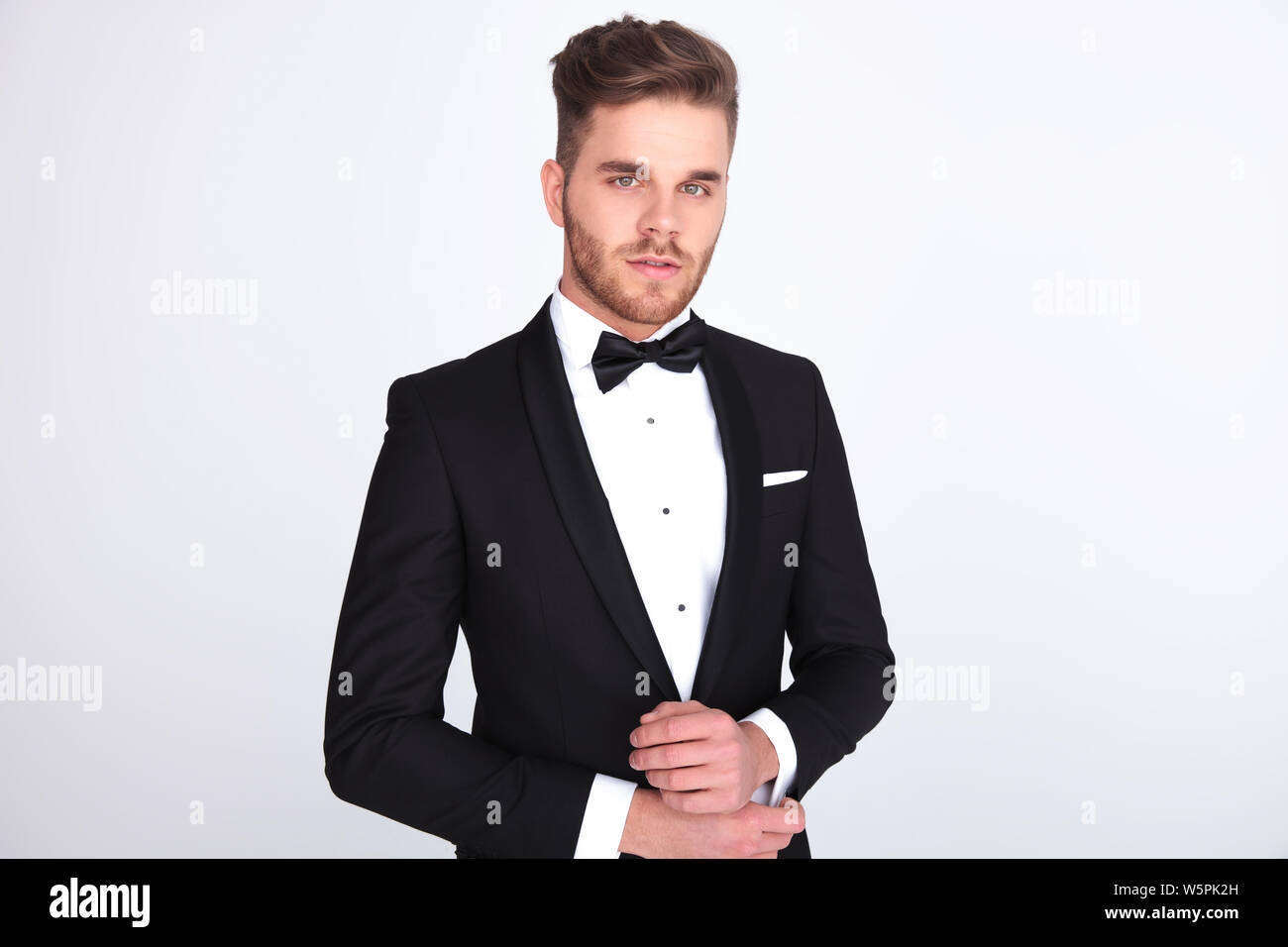 portrait of young elegant man in black tuxedo fixing his links while ...