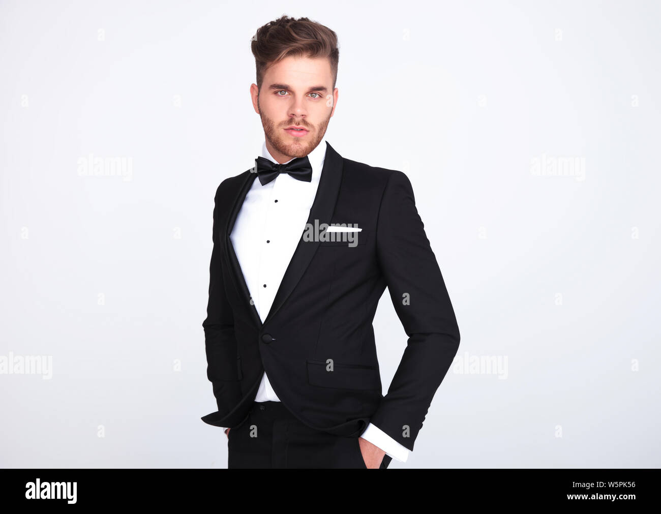 portrait of relaxed elegant man in black tuxedo standing on light grey ...