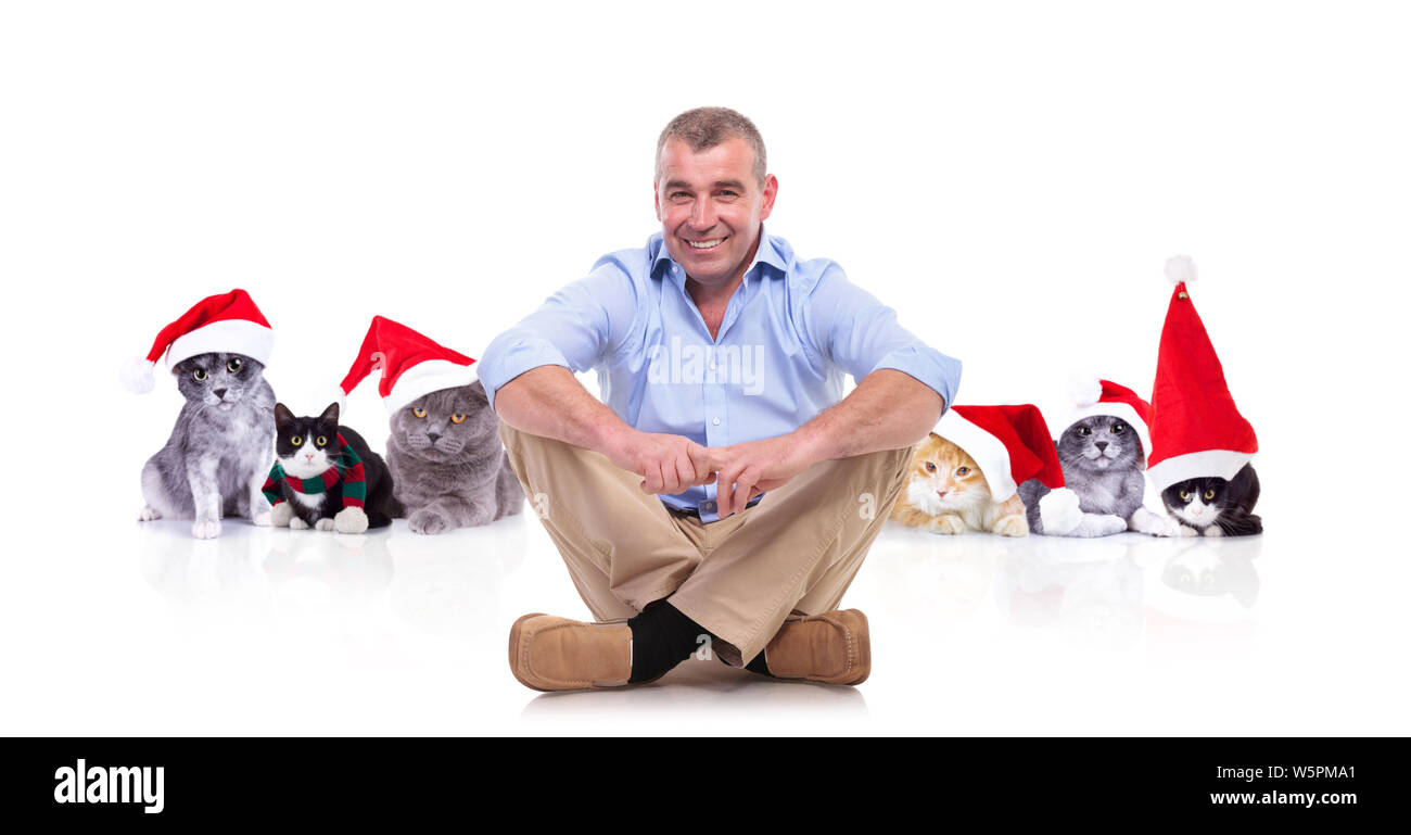 mature man sitting cross-legged in front of team of christmas cats on white background and smiling Stock Photo