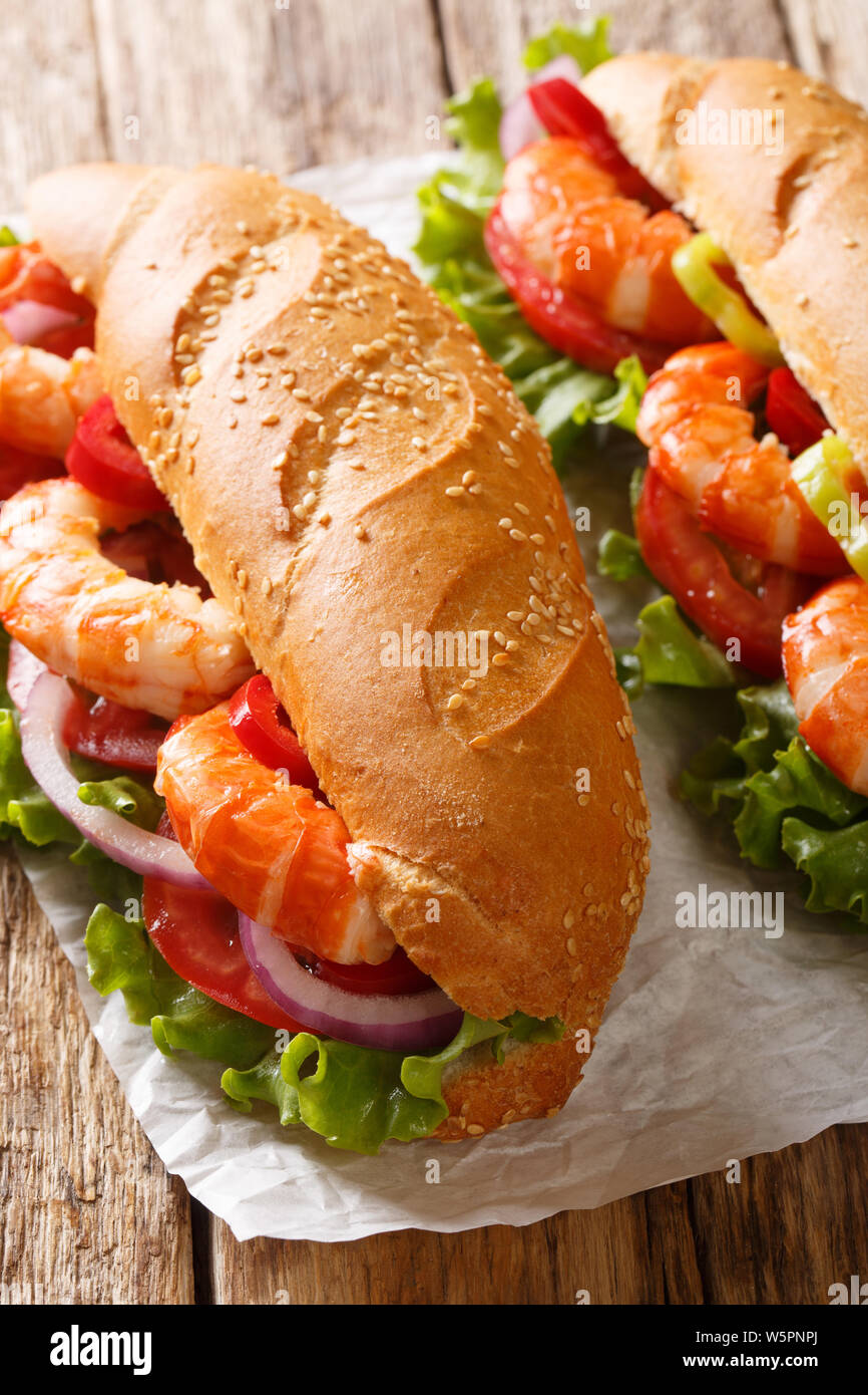 Sandwich with shrimps, tomatoes, peppers, onions and fresh lettuce close-up on parchment on the table. vertical Stock Photo
