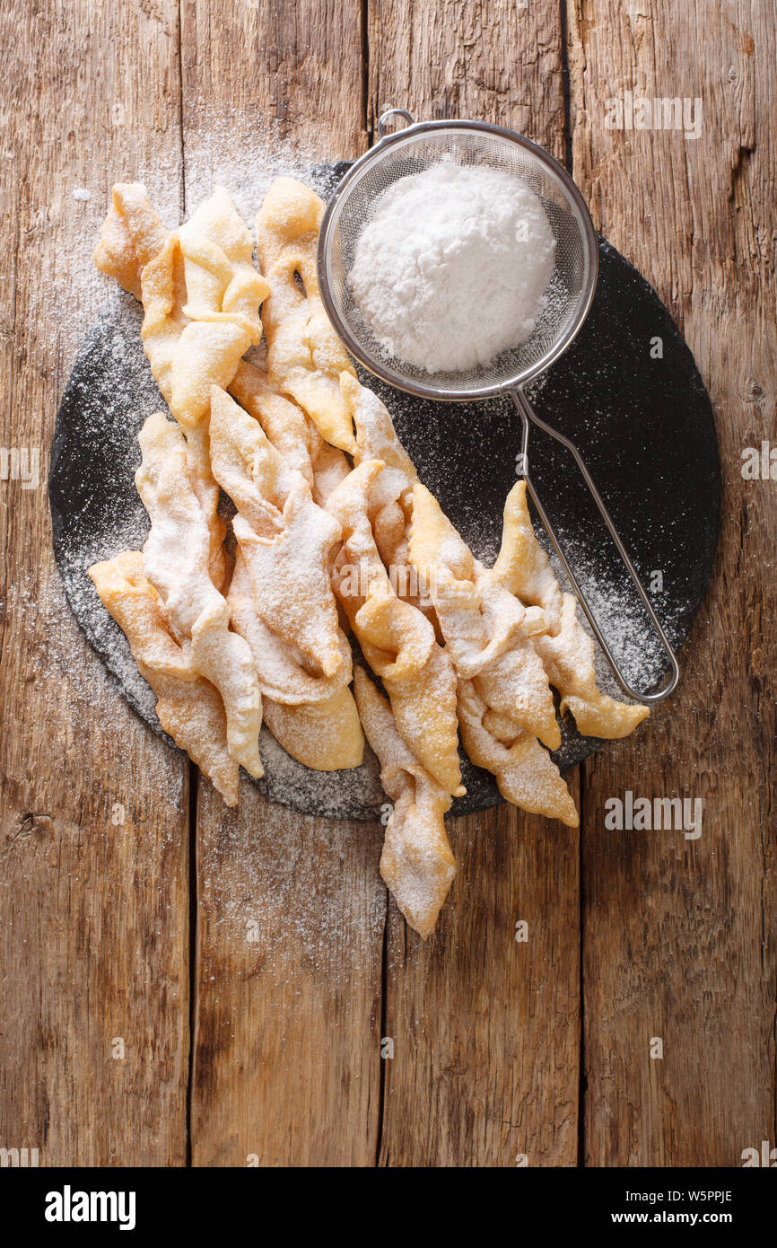 Traditional dessert Angel Wings Dusted with powdered sugar close-up on the table. Vertical top view from above Stock Photo