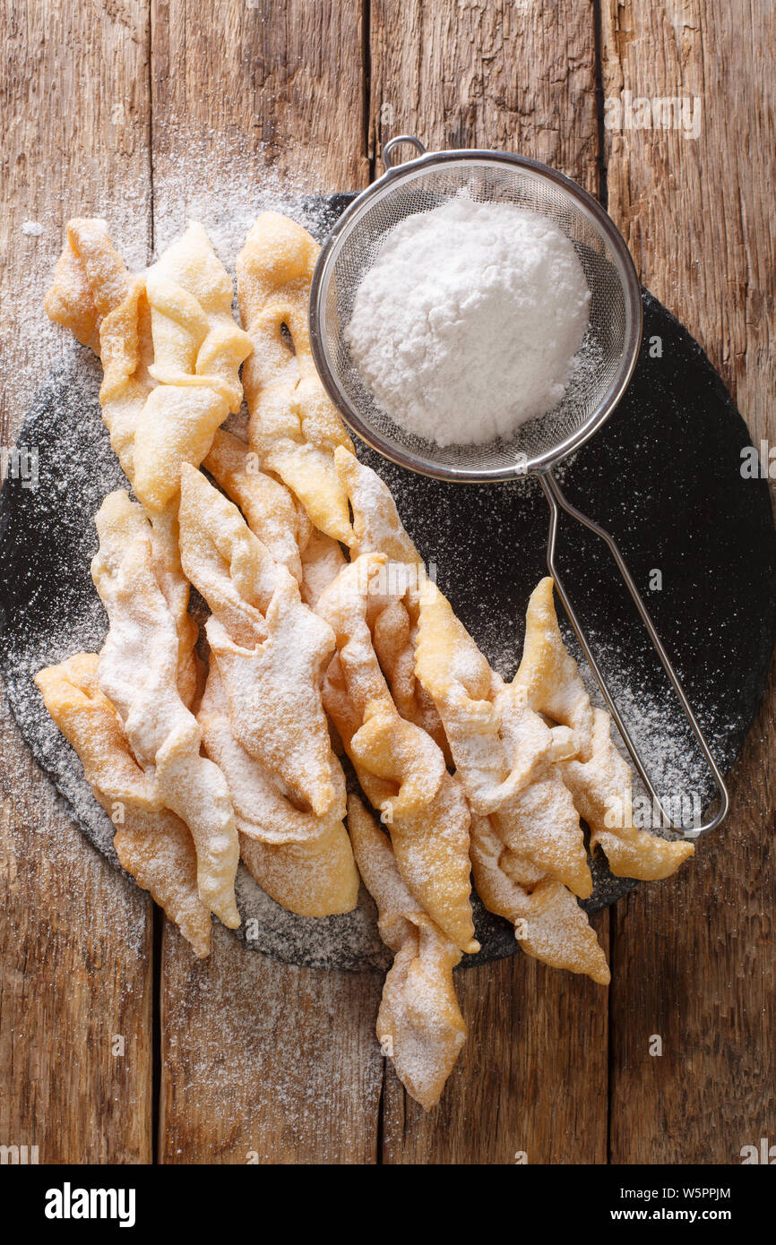 Freshly made Angel Wings Cookies with powdered sugar close-up on the table. Vertical top view from above Stock Photo