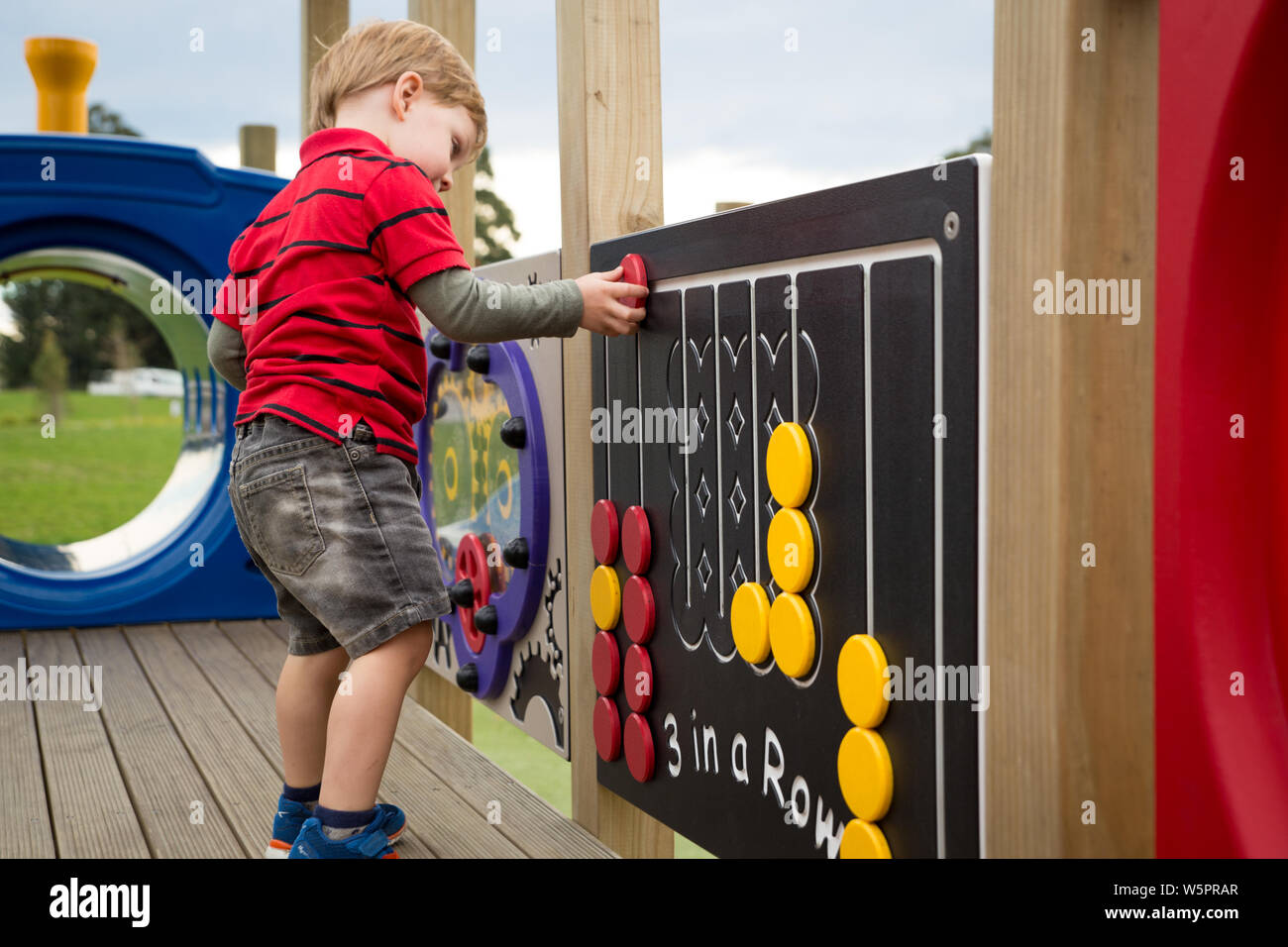 A young preschool child plays with the activities attached to the climbing frame at the new Foster Park Playground in Rolleston, New Zealand Stock Photo