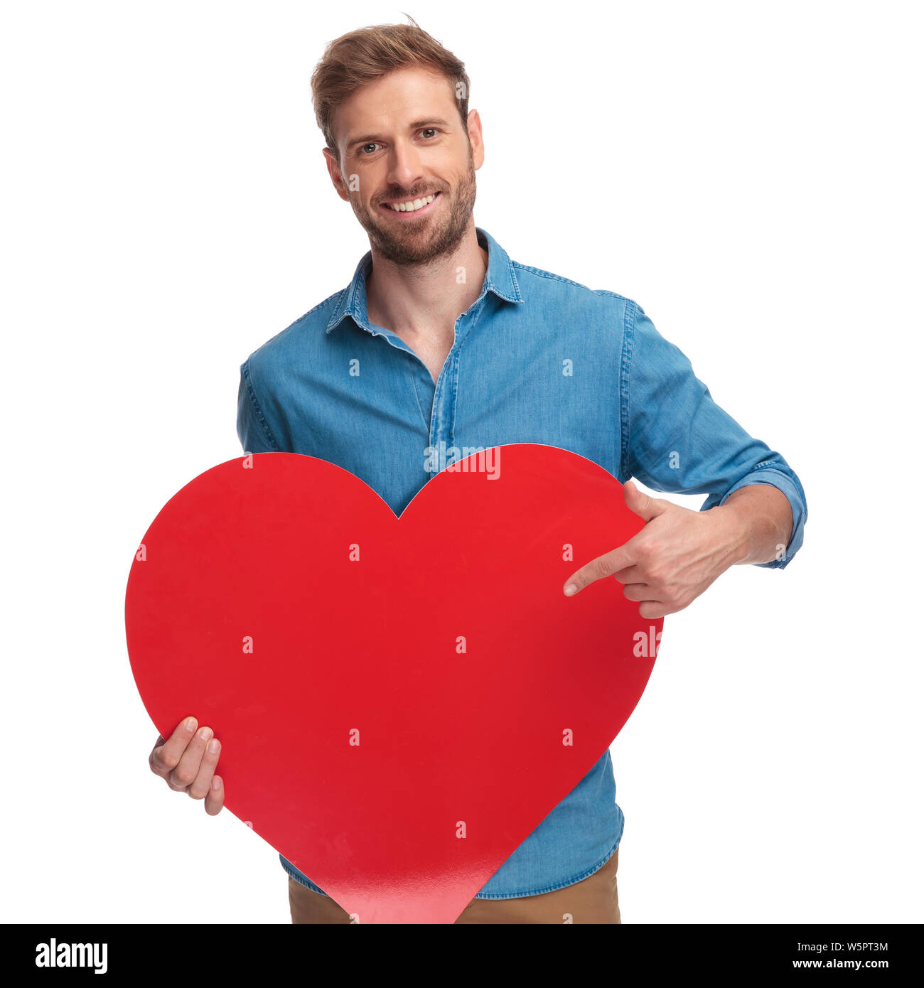 smiling casual man holding red heart and points finger at it on white ...