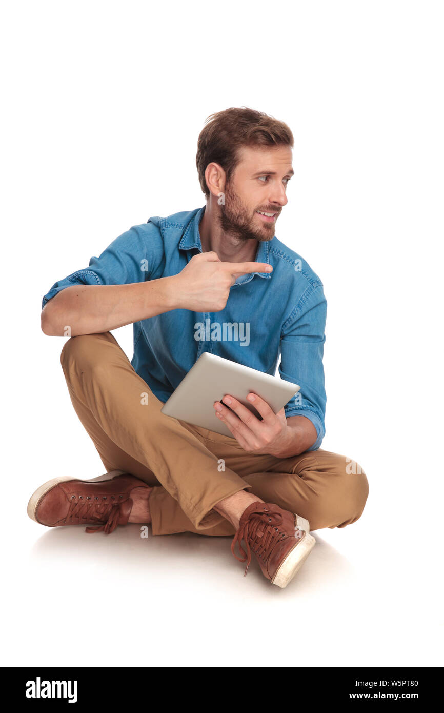 seated young casual man with tablet points to side on white background Stock Photo