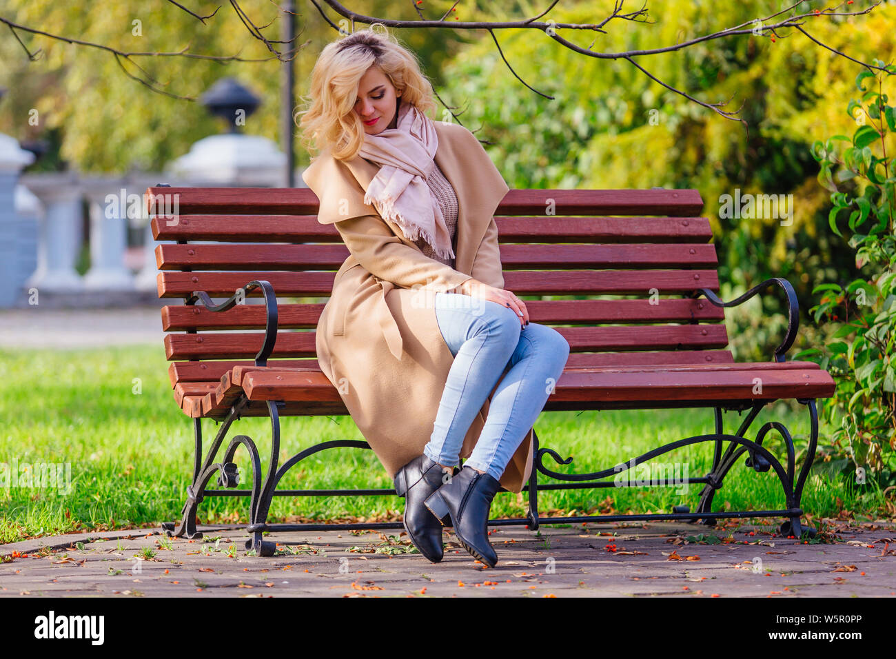 Young beautiful woman sitting on the bench in autumn park under the ...
