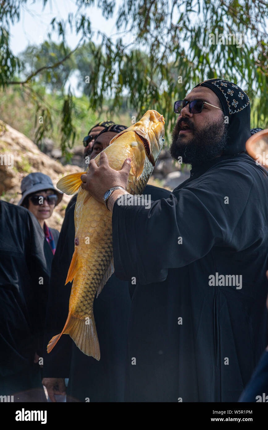 Tabgha, Israel - May 18 2019 : Coptic monk at Tabgha church beside Sea of Galilee holding a big fish Stock Photo
