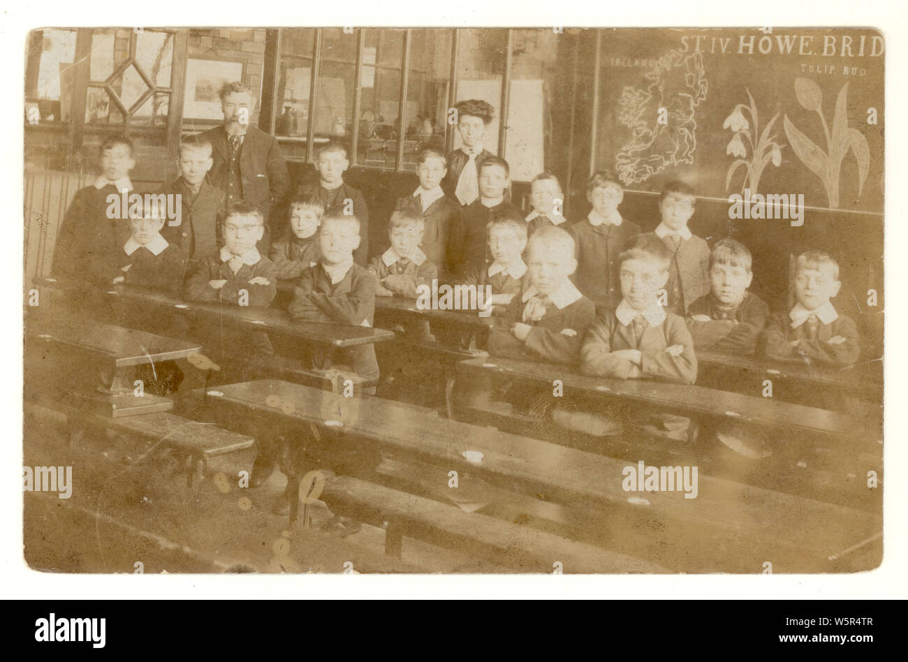 Faded Edwardian postcard of schoolboys in classroom, map of Ireland, tulip and snowdrop on the blackboard, strict school mistress in background,possibly St Michaels C E Primary School, Howe Bridge, Manchester  U.K. circa 1906 Stock Photo