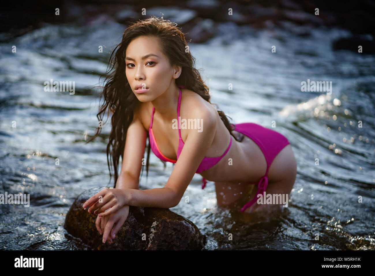 Concept: tourism, holidays, travel. Young lean pretty asian girl in two pieces pink swimsuit relax on seashore. Fashion photoshoot. Stock Photo