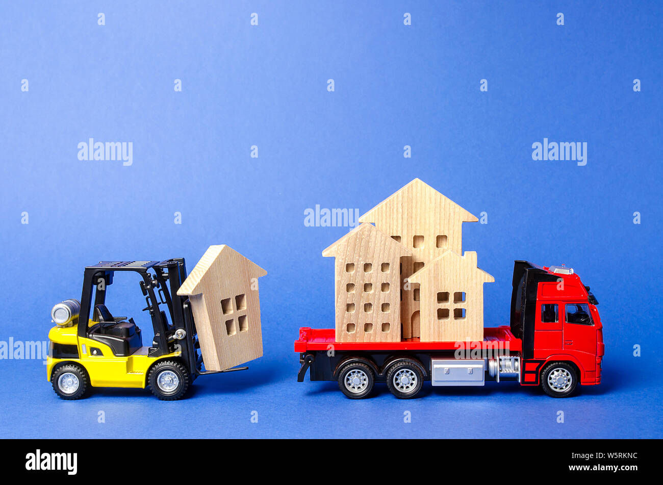 A yellow forklift loads a house figures on a red truck. Concept of transportation and cargo shipping, moving company. Construction of new houses and o Stock Photo