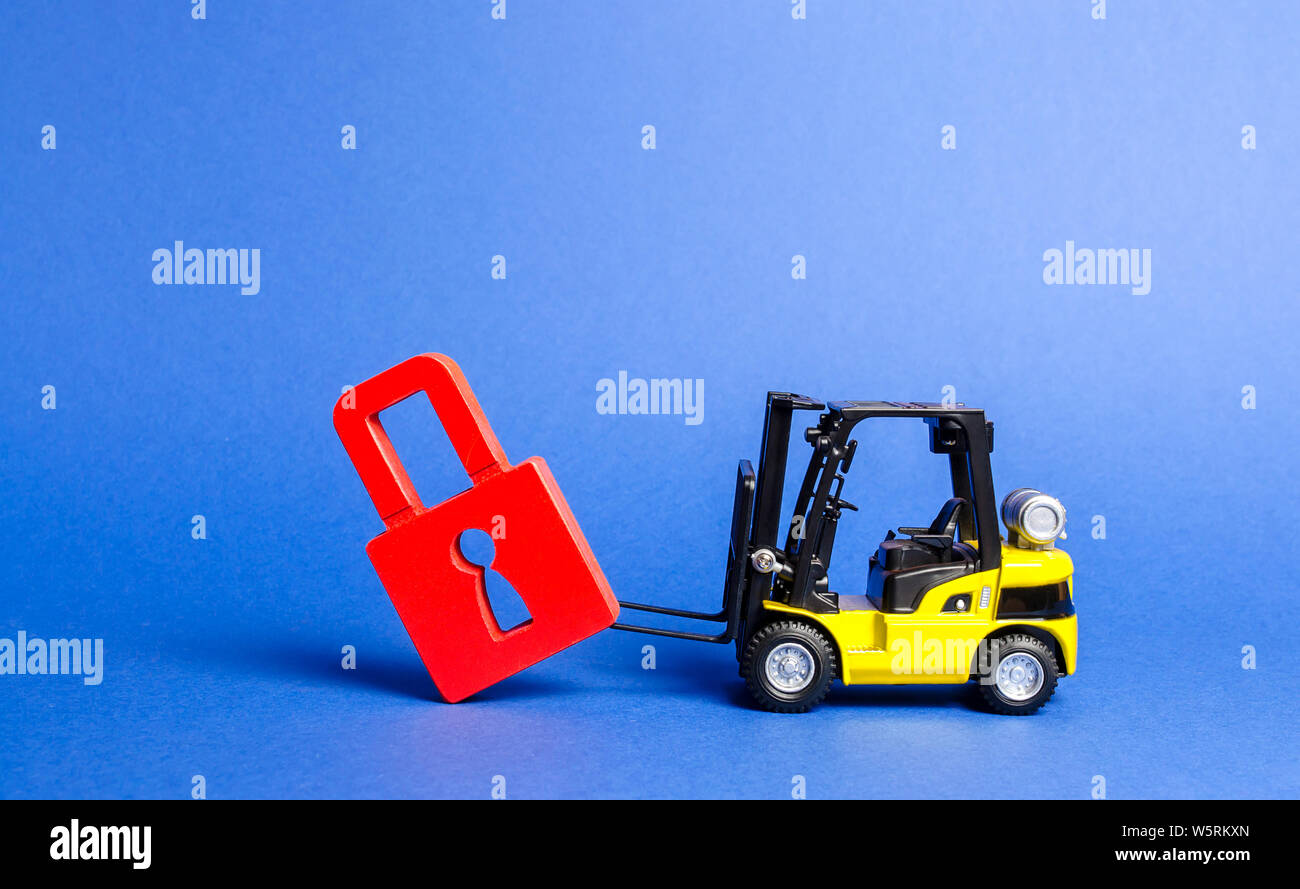 A yellow forklift tilts a red padlock from the road. Bypassing prohibitions and sanctions restrictions, lobbying the interests of industry in governme Stock Photo