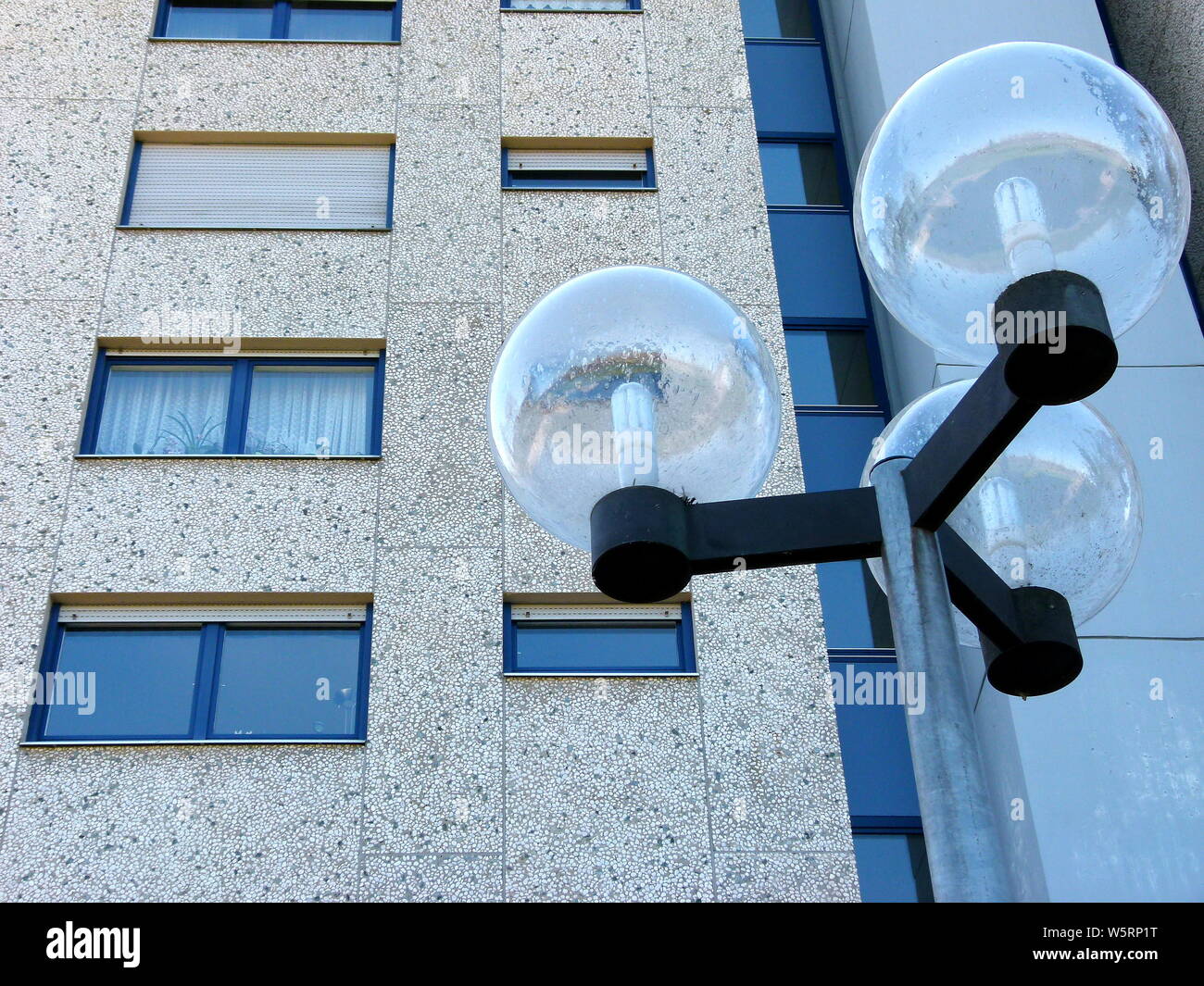 3-armed street lamp with modern glass ball in front of gray skyscraper facade Stock Photo
