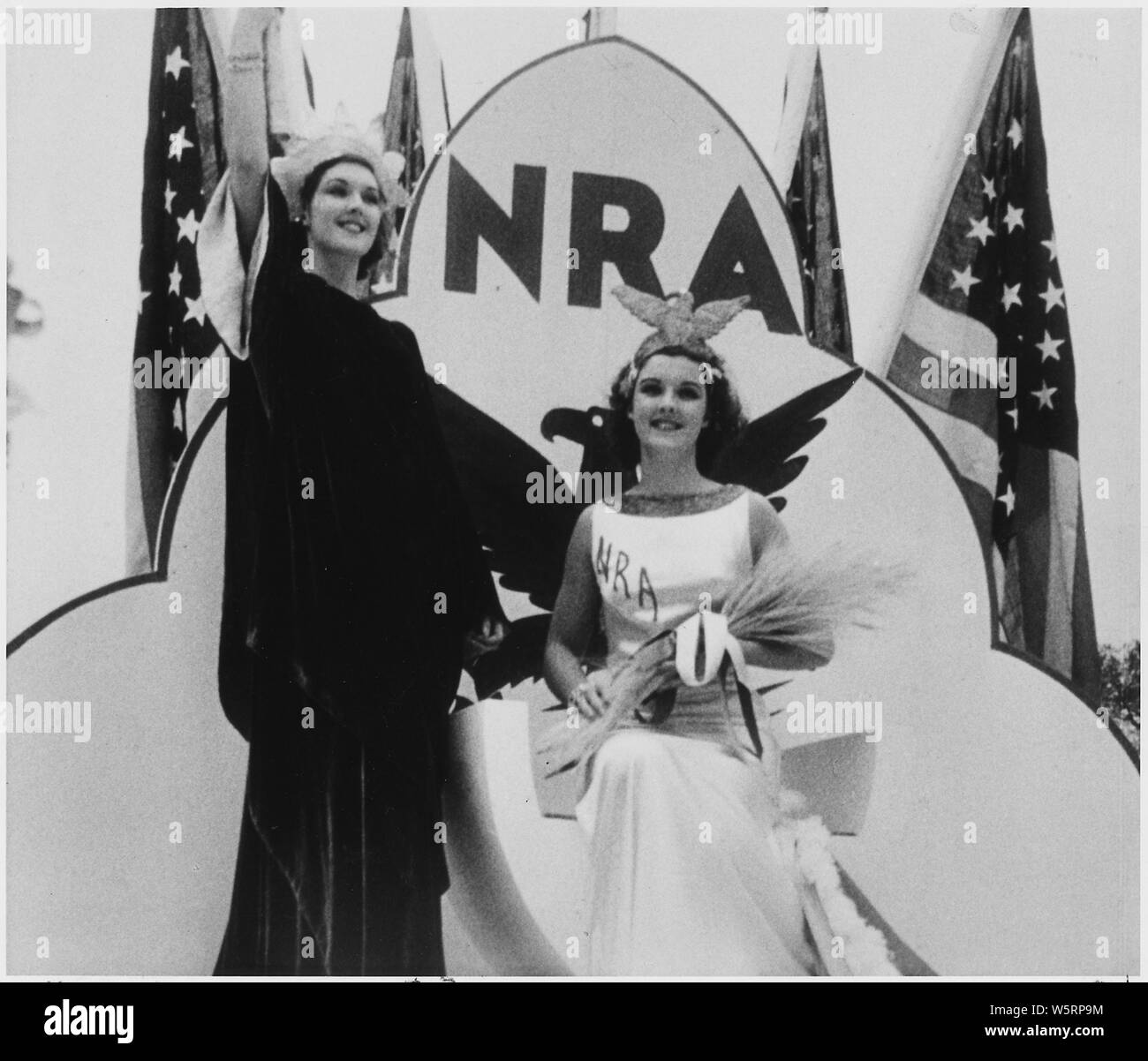 NRA:posed shot of two woman dressed in costumes promoting National Recovery Administration programs with blue eagle emblem, NRA letters, and American flags in background Stock Photo