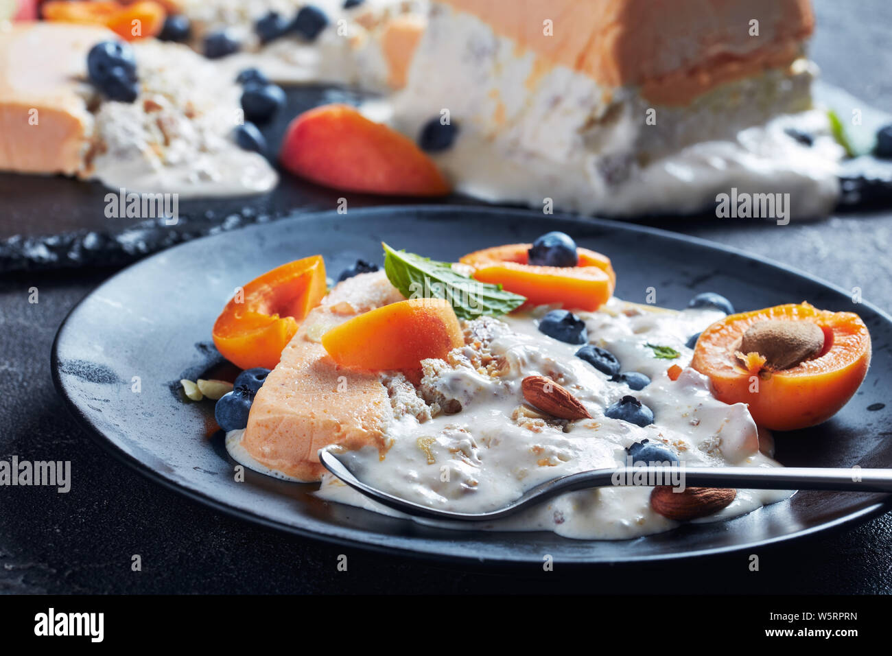 Italian summer dessert, Sicilian Almond apricot melon Semifreddo served on a black plate with fruits and berries, view from above, close-up Stock Photo