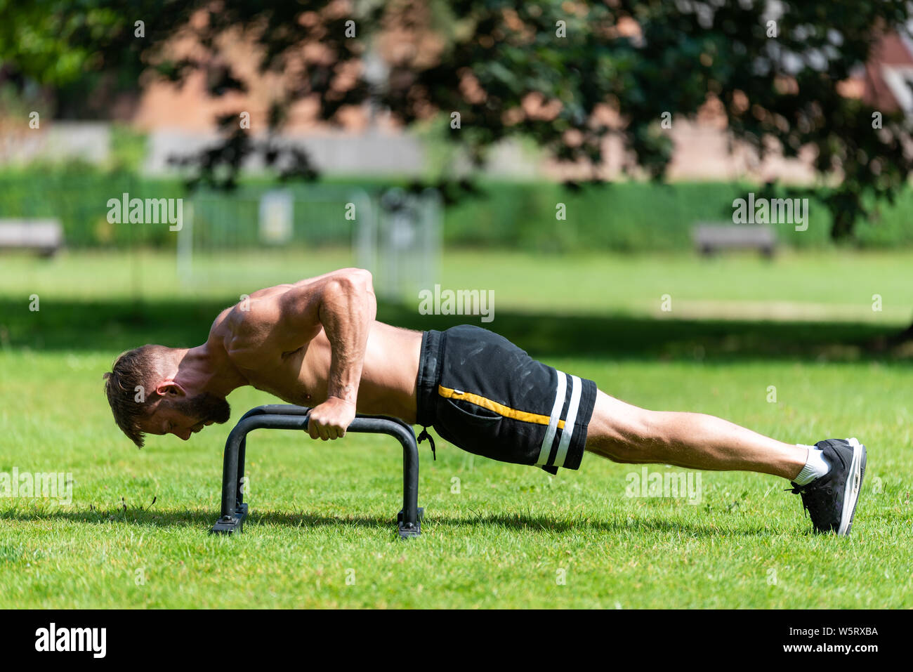 Fit athlete man doing push up with push-up bars on the floor, outdoor ...