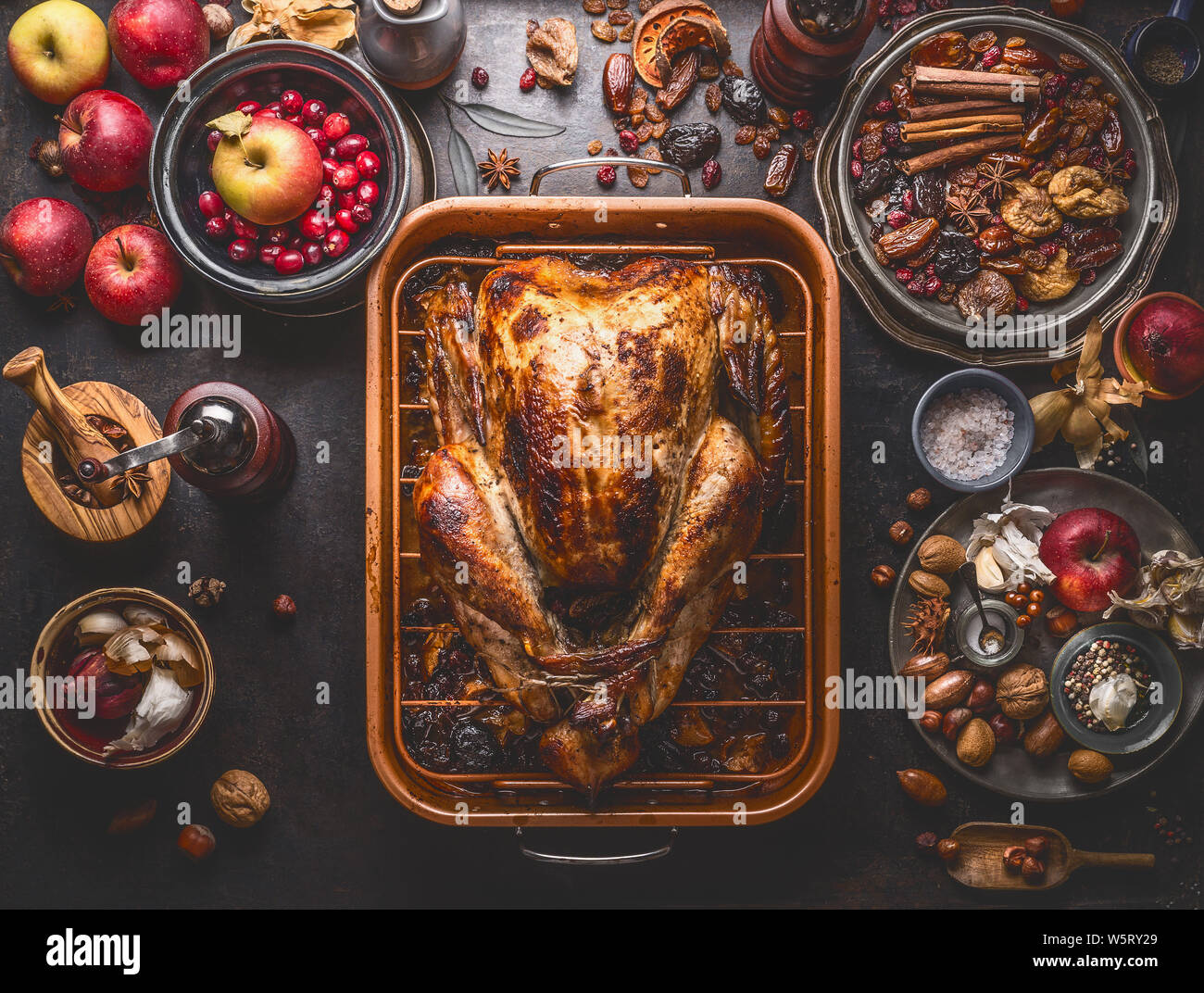 Whole roasted stuffed turkey in baking tray to Thanksgiving dinner on kitchen table with various autumn seasonal ingredients: apples, cranberries, var Stock Photo