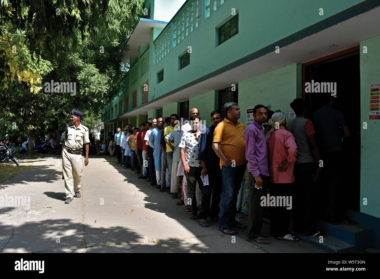 Patna, Bihar, India - May 19, 2019: People queue up to cast their precious votes as a security-personnel walks by ensuring law and order. Stock Photo