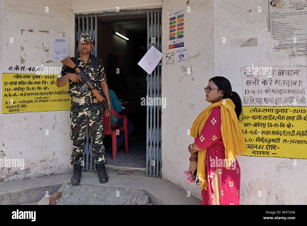 Patna, Bihar, India - May 19, 2019: A security personnel guards the ballot room while a voter awaits her turn outside the polling booth. Stock Photo