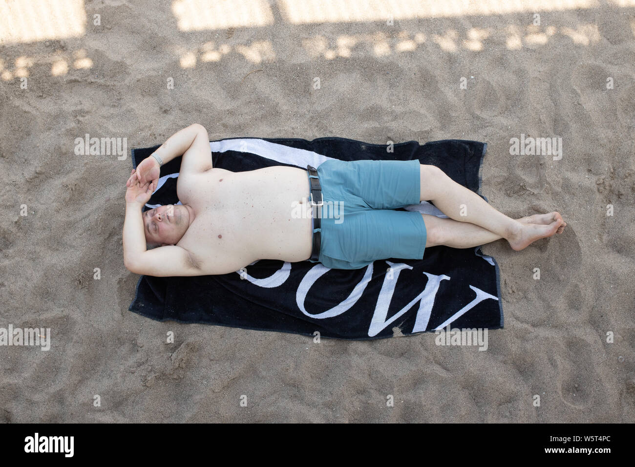 Hot weather in Skegness. A man shelters in the shade of Skegness pier on the hottest day of the year Stock Photo