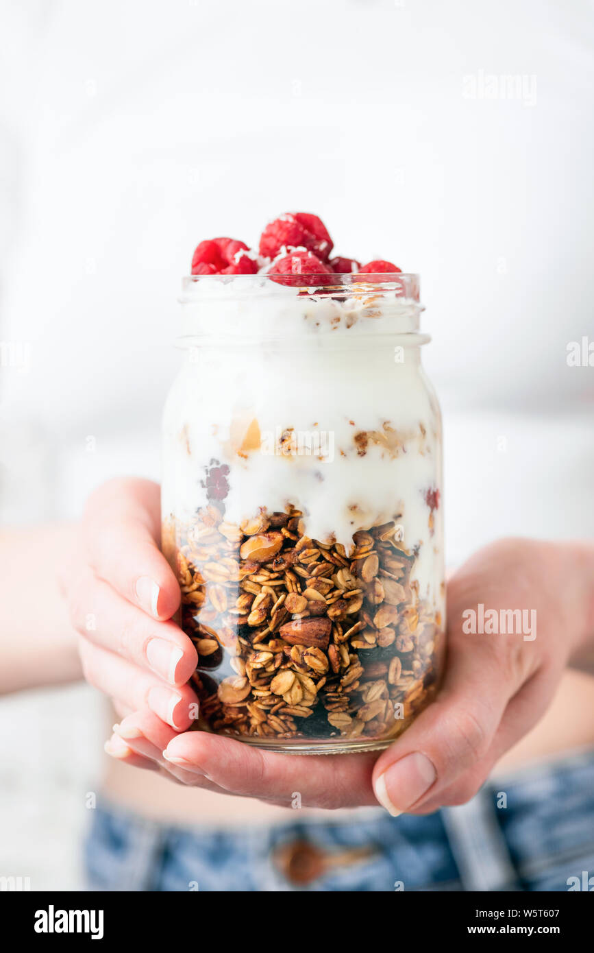 Yogurt with raspberry and oat granola in a jar in girl's hands. Clean
