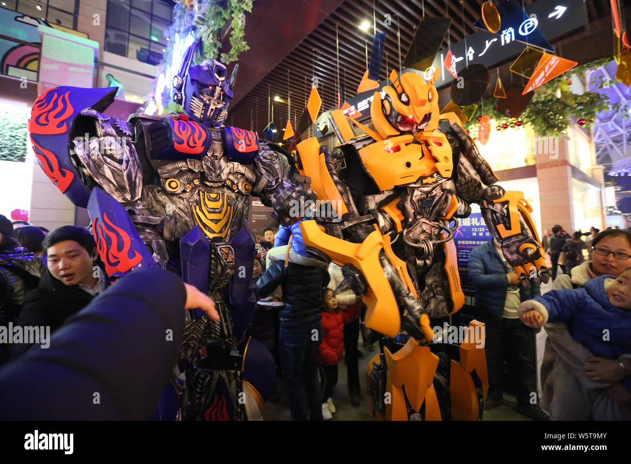 College students wearing two-meter-high life-size replicas of Megatron and Bumblebee are surrounded by customers at a shopping mall in Xi'an city, nor Stock Photo