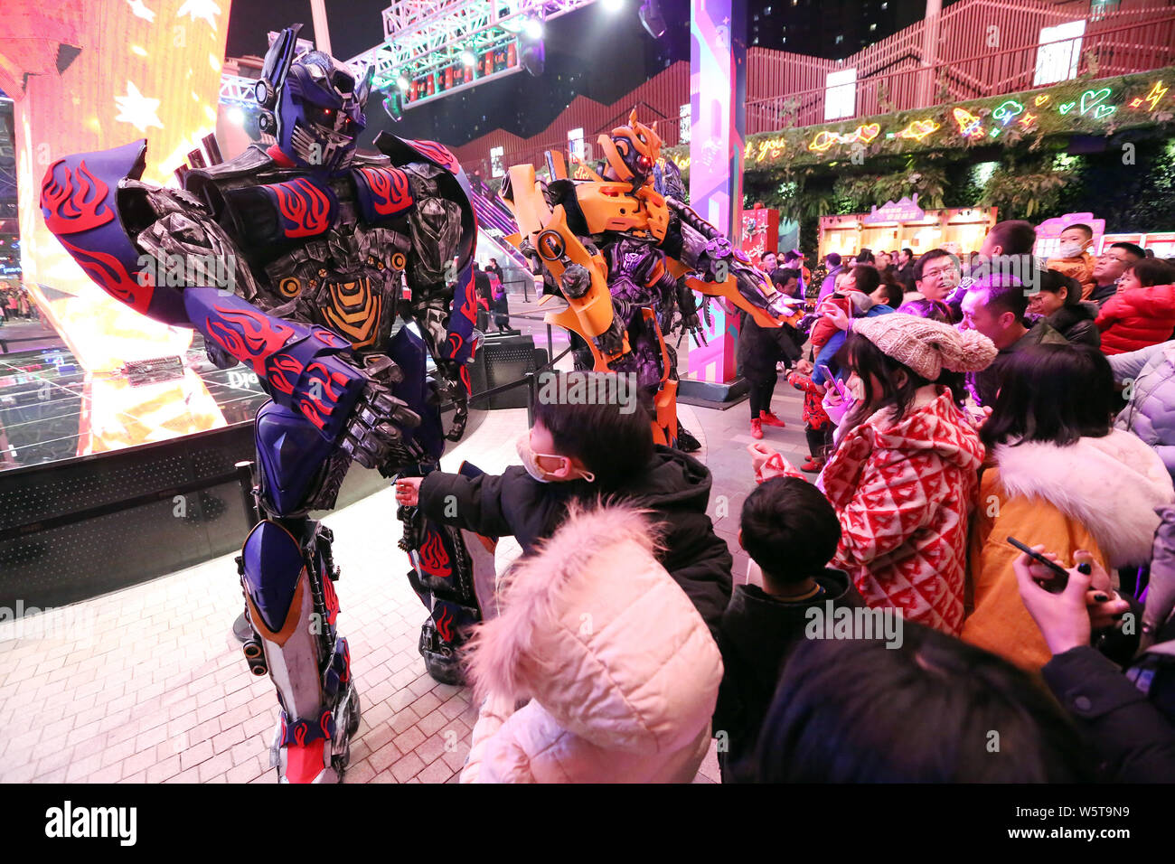 College students wearing two-meter-high life-size replicas of Megatron and Bumblebee are surrounded by customers at a shopping mall in Xi'an city, nor Stock Photo
