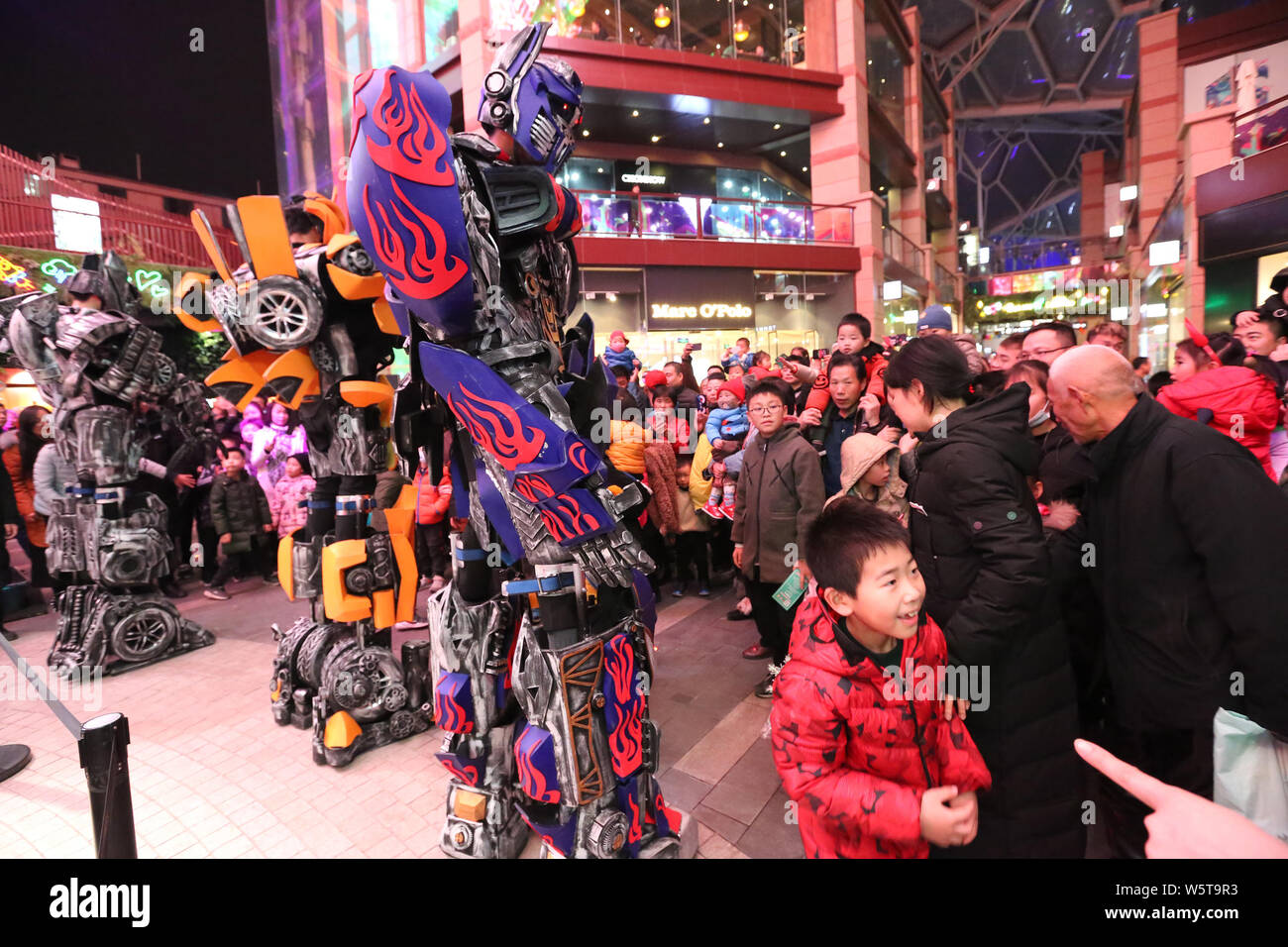 College students wearing two-meter-high life-size replicas of Megatron, Optimus Prime and Bumblebee are surrounded by customers at a shopping mall in Stock Photo