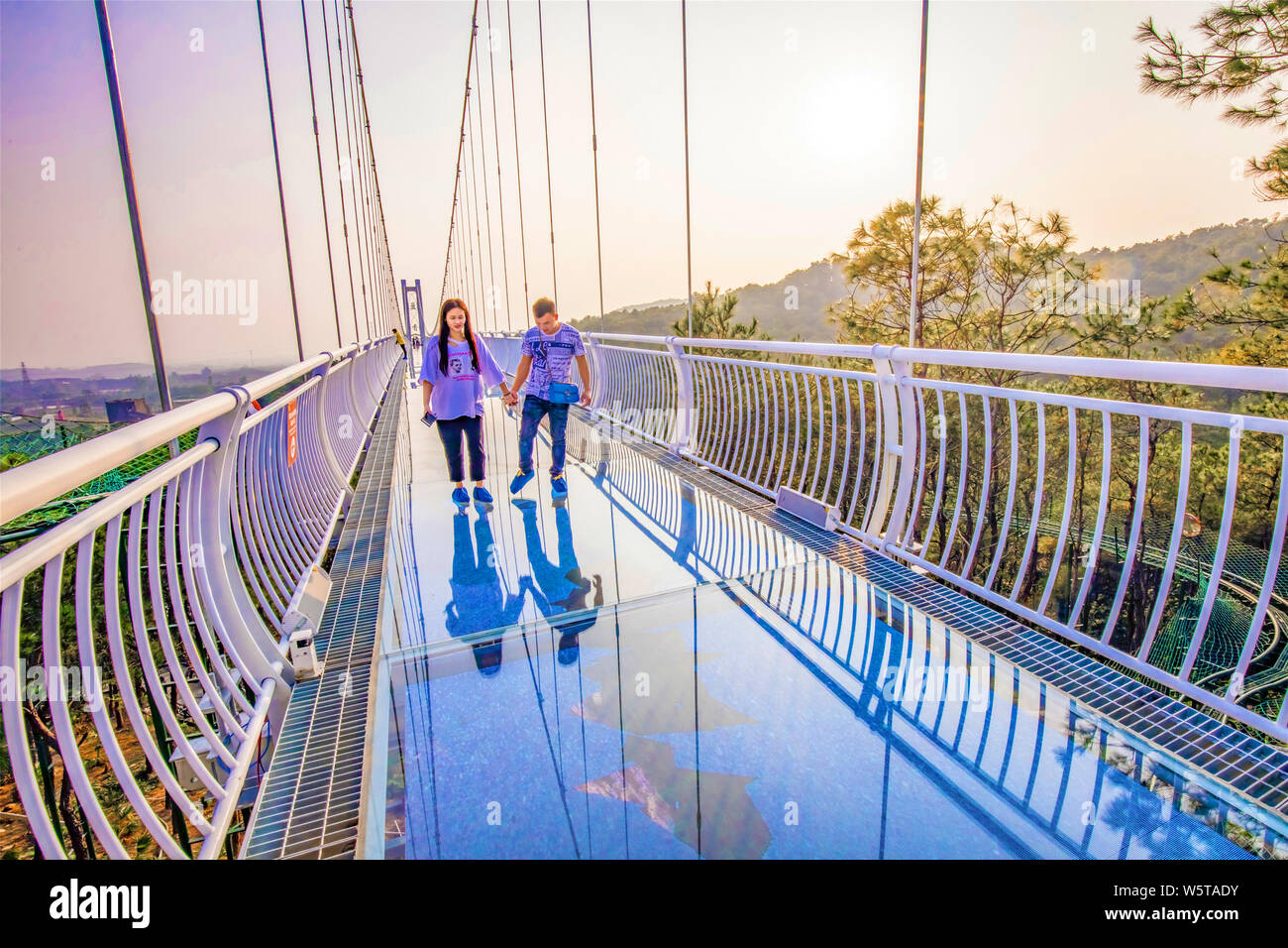 Tourists pose for photos on a glassbottomed bridge at sunset in Foshan