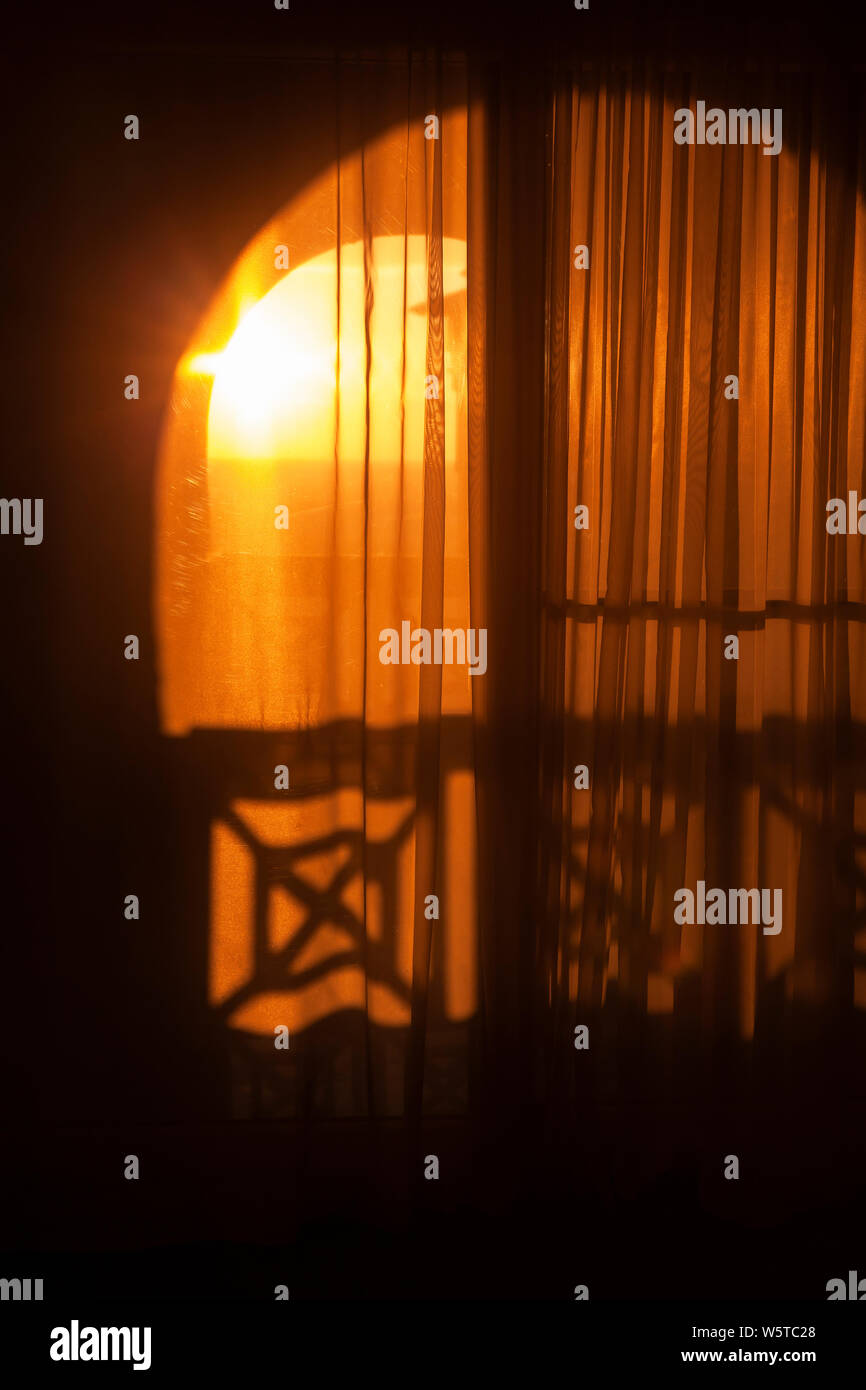 Abstract interior fragment, vertical background photo. Arch of the balcony door with transparent tulle and glowing sun outside Stock Photo