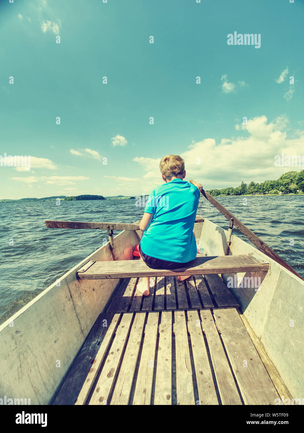 Young teenage boy rowing a rowboat or paddle boat on a lake with forest