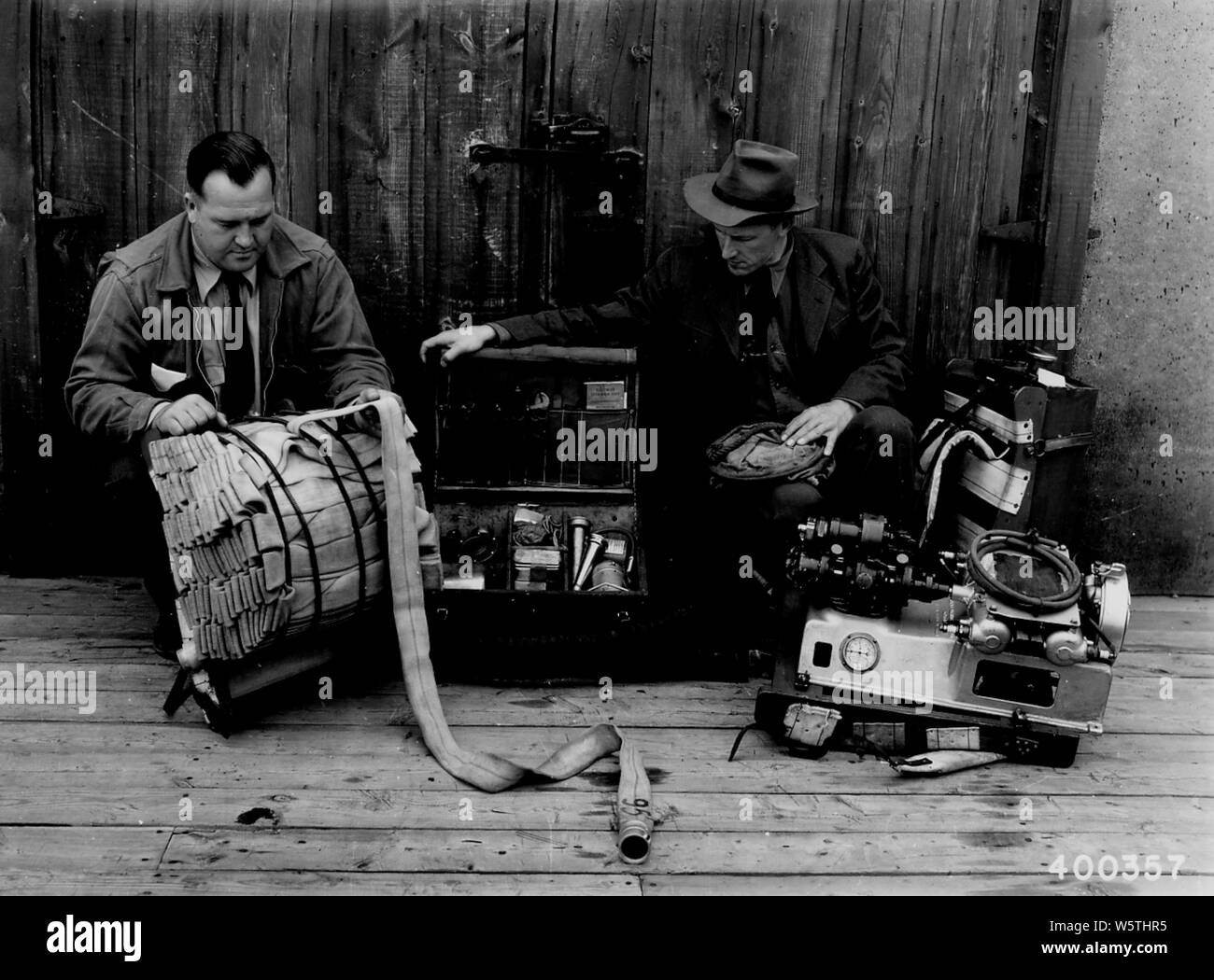 Photograph of Display of Portable Power Pump Unit; Scope and content:  Original caption: Display of Portable Power Pump Unit (Pac.Marine Type N) at the fire cache bldg., Gegoka CCC Camp. L.toR. 400' of hose, accessory box, pump and can of gasoline. Note the form fitting pack frames to which these items are fastened. Detailed data regarding ea. Stock Photo