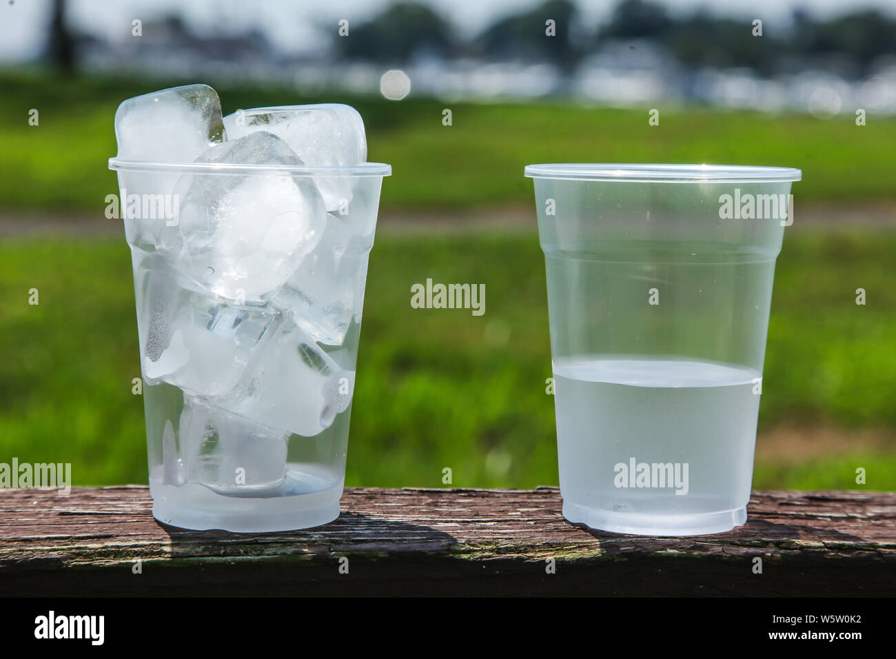 Cup full of ice with a second image of cup half full of water to show the ice melted outdoor Stock Photo