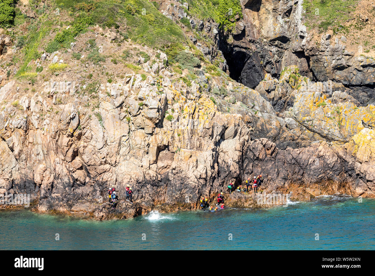 A group of young people coasteering below the cliffs at Pointe de la Moye, Le Gouffre, Les Villets on the beautiful, rugged south coast of Guernsey UK Stock Photo