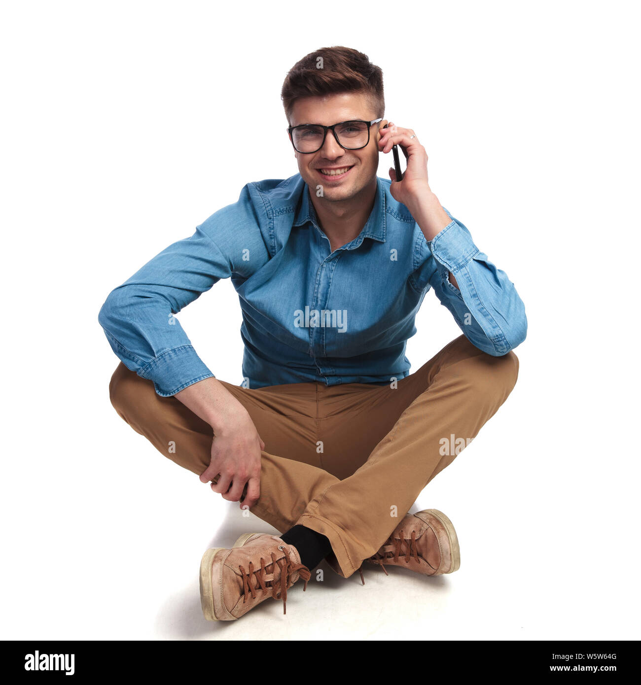 casual man sits on the floor and talks on the phone on white background ...
