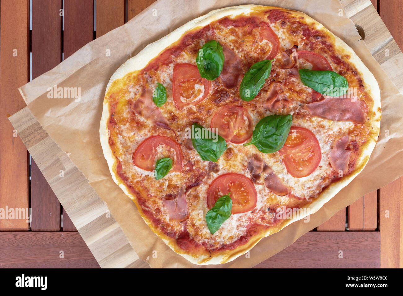 top view of fresh homemade pizza with serrano ham, sliced tomatoes and ham on wooden garden table Stock Photo