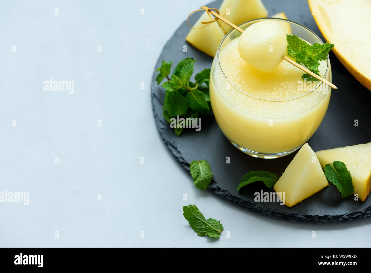 Cold fresh melon smoothie with melon ball and mint leaves on gray wooden background. Summer drink. Healthy food concept. Soft focus Stock Photo