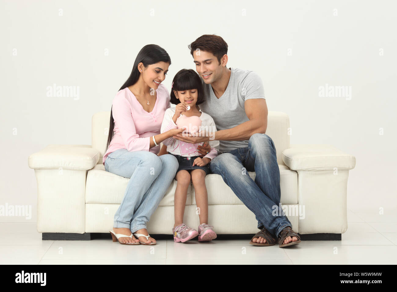 Girl putting coin into a piggy bank with her parents Stock Photo - Alamy