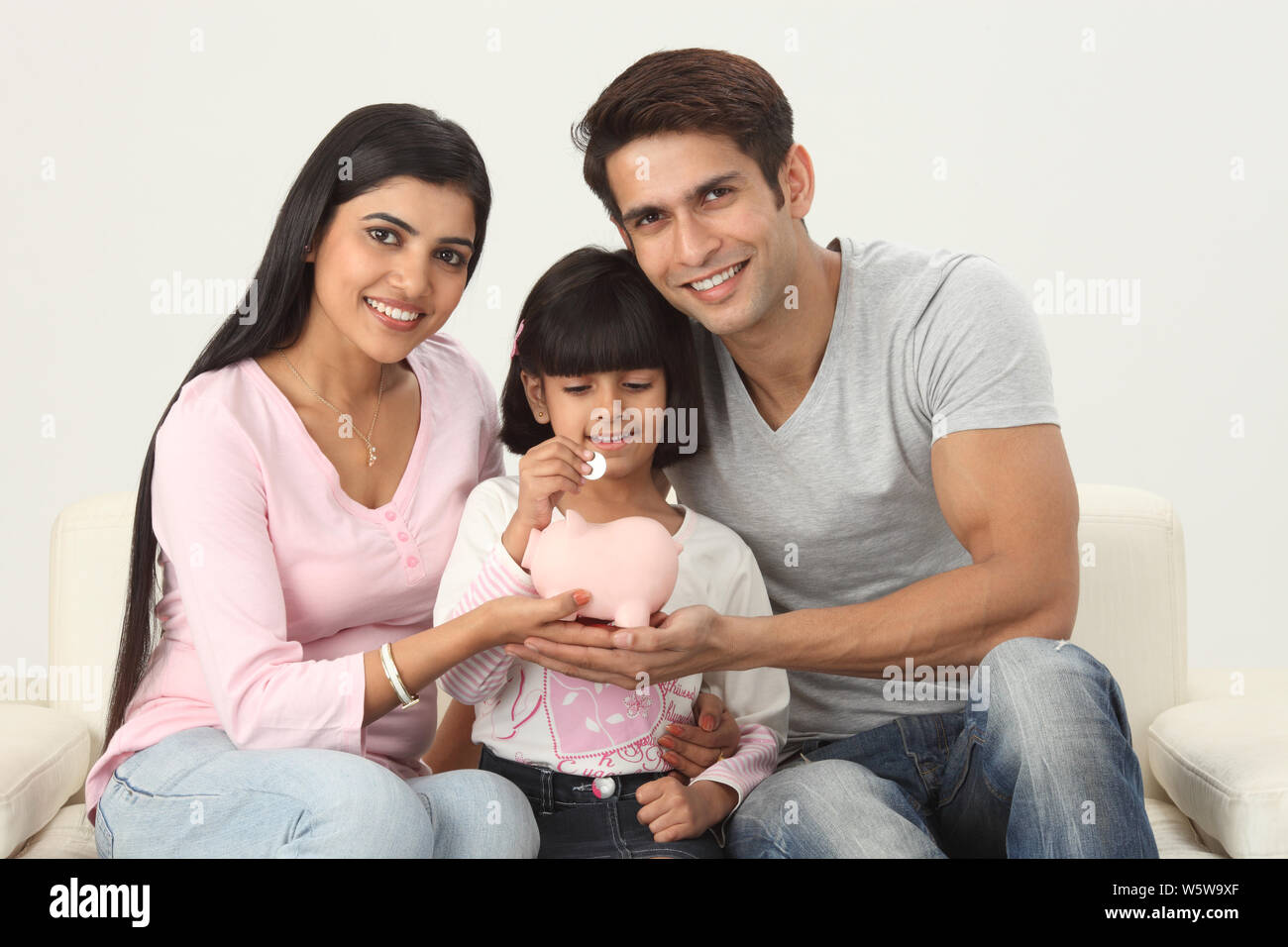 Indian girl putting coin into a piggy bank with her parents Stock Photo ...