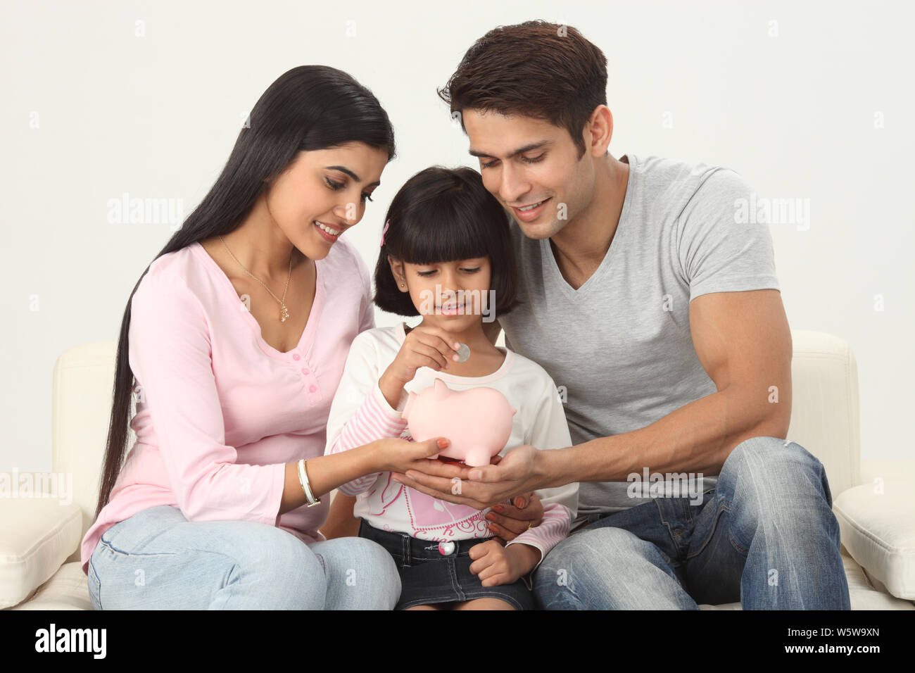 Girl putting coin into a piggy bank with her parents Stock Photo - Alamy
