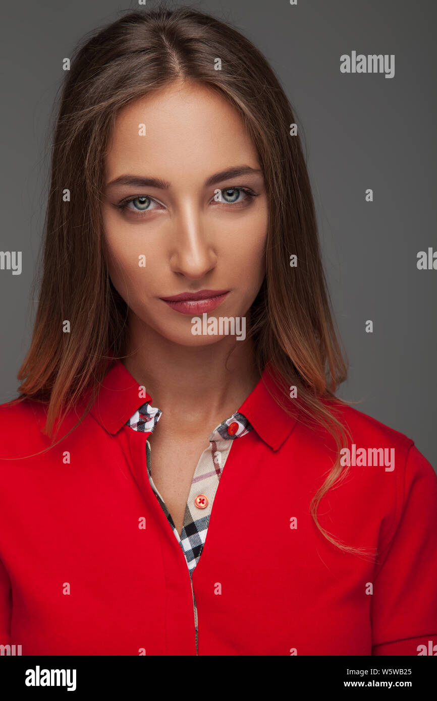 cool young woman with blue eyes wearing red polo shirt on grey background Stock Photo