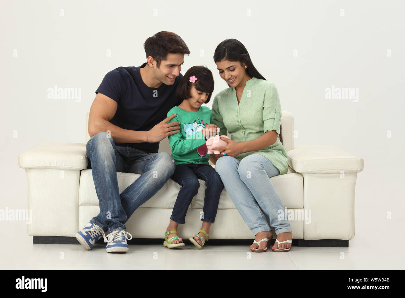 Girl putting coin into a piggy bank with her parents Stock Photo - Alamy