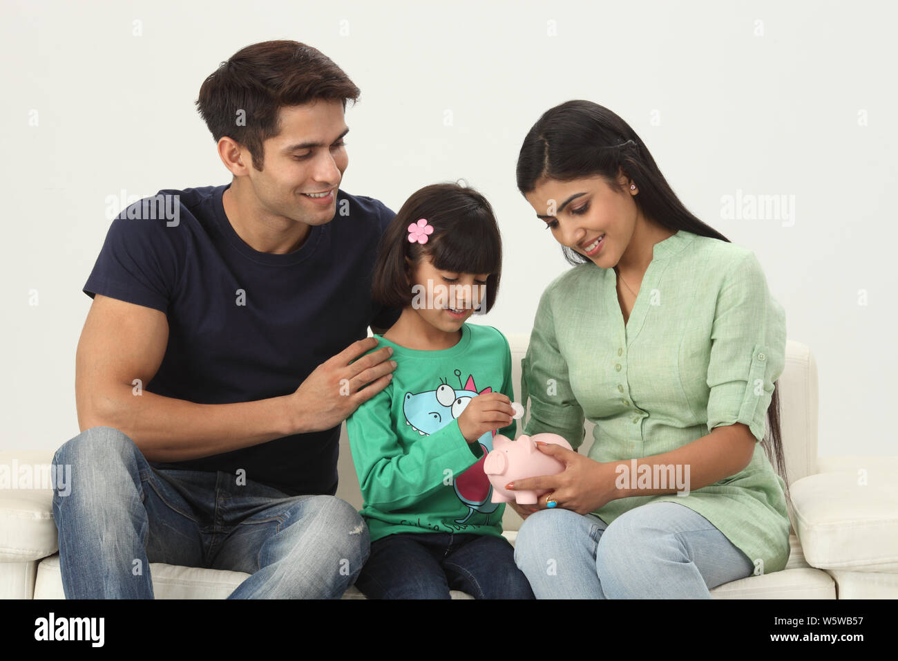 Girl putting coin into a piggy bank with her parents Stock Photo - Alamy
