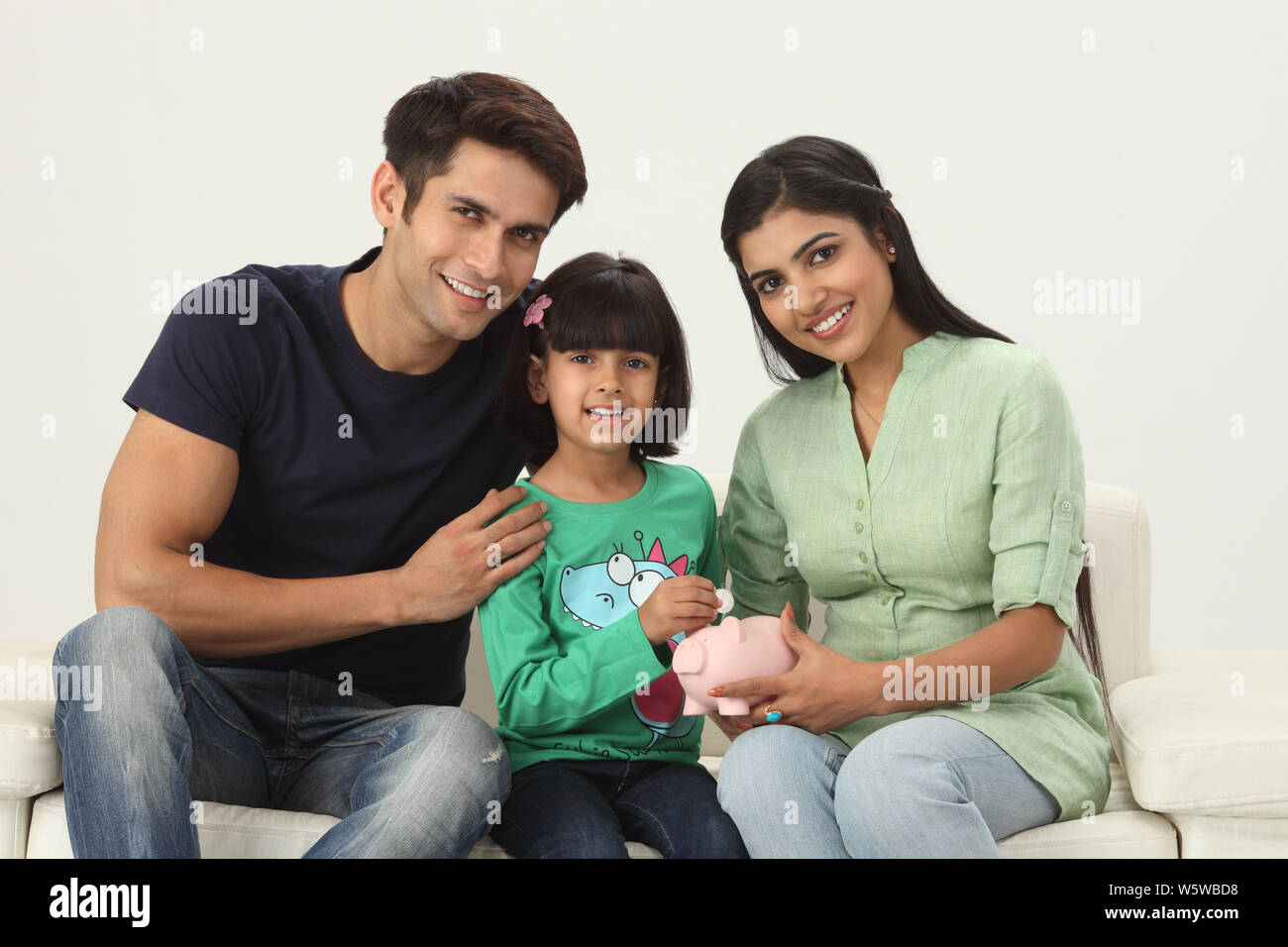 Girl putting coin into a piggy bank with her parents Stock Photo - Alamy