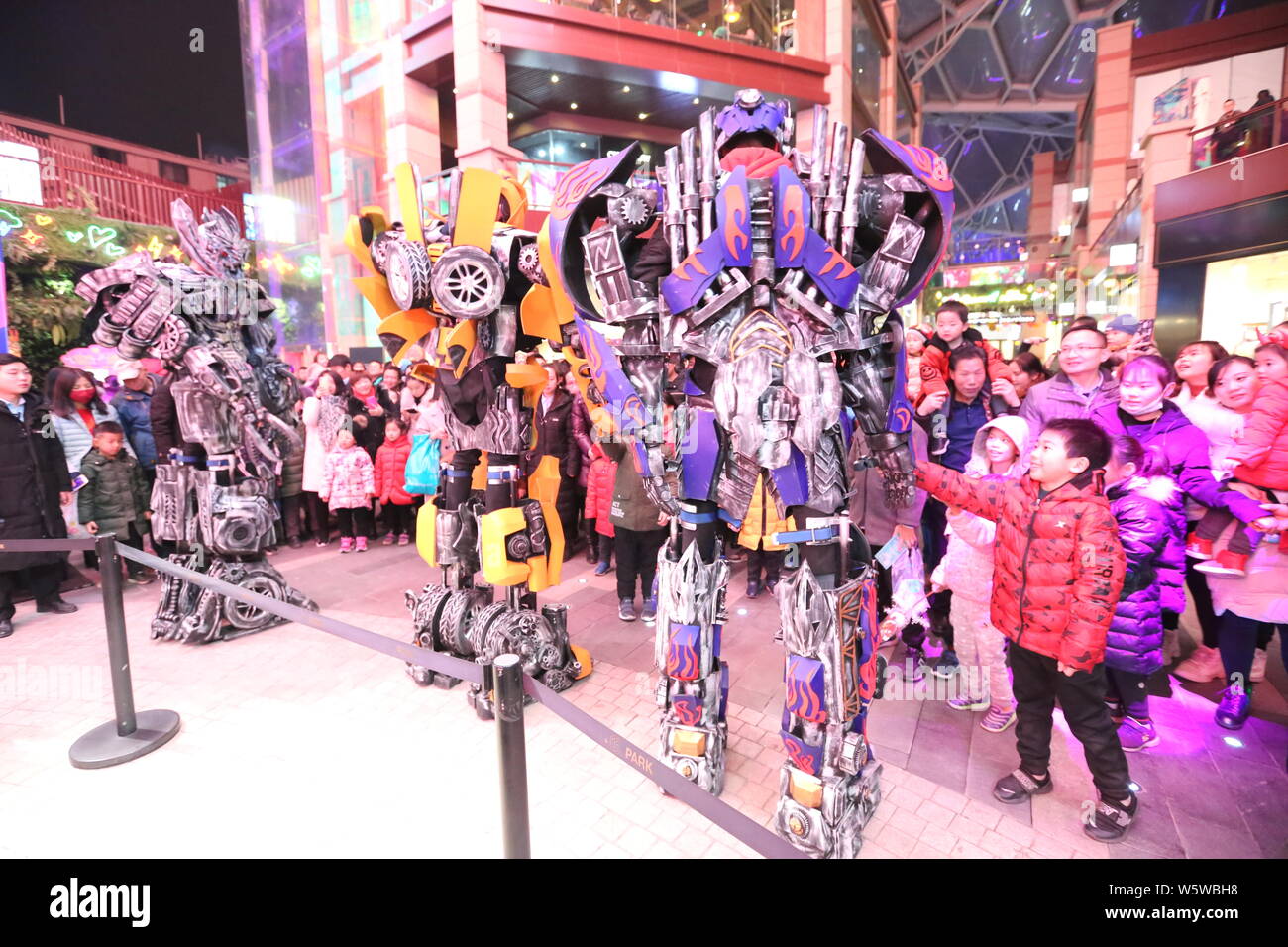 College students wearing two-meter-high life-size replicas of Megatron, Optimus Prime and Bumblebee are surrounded by customers at a shopping mall in Stock Photo