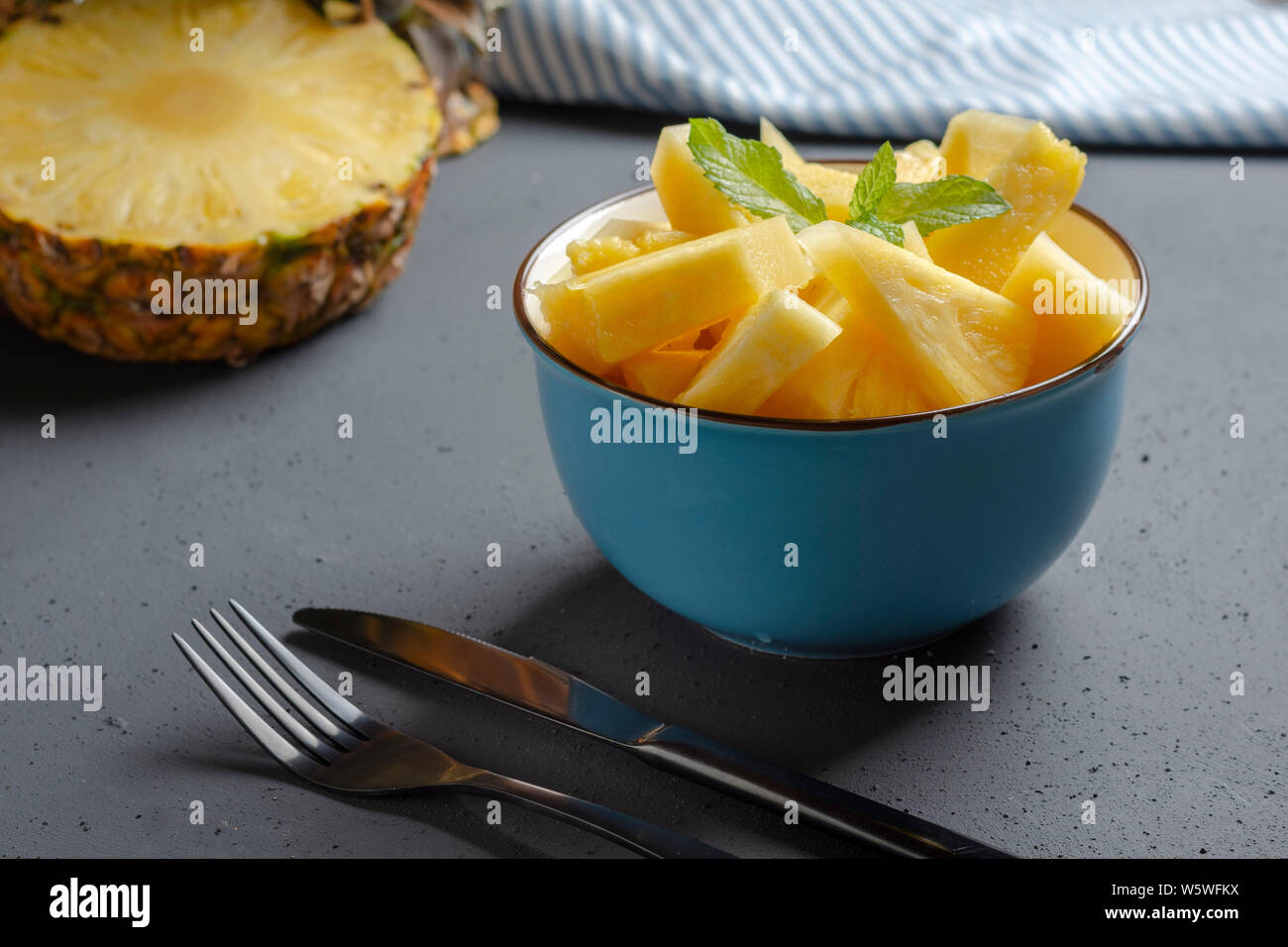 Blue bowl with fresh pineapple on rustic black background with cutlery Stock Photo