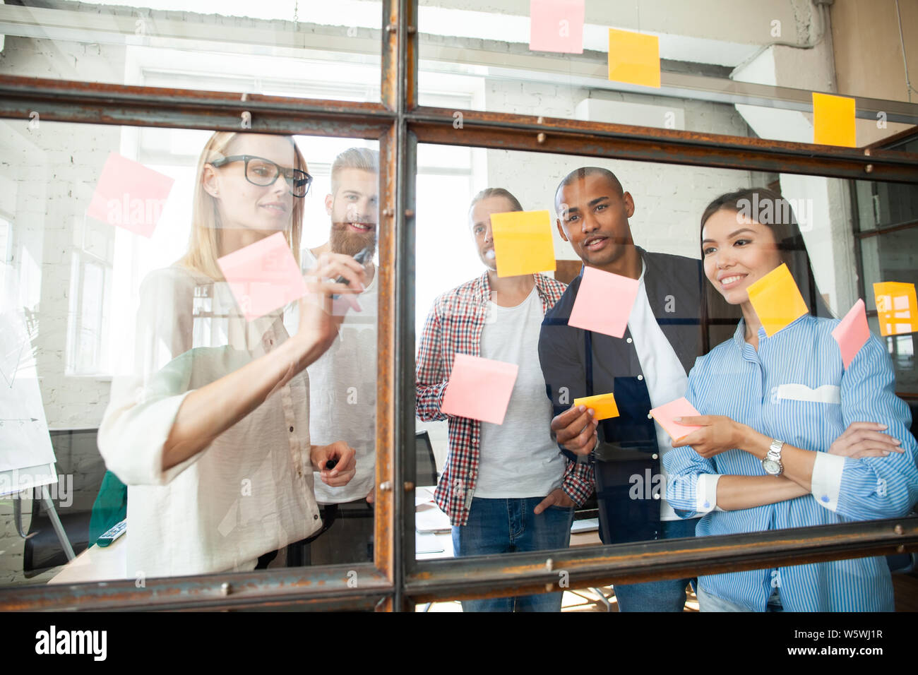 Young modern people in smart casual wear using adhesive notes while