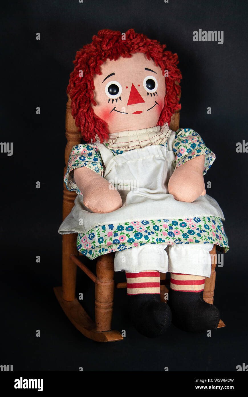 old rag doll with white apron sitting in a wooden rocking chair Stock Photo