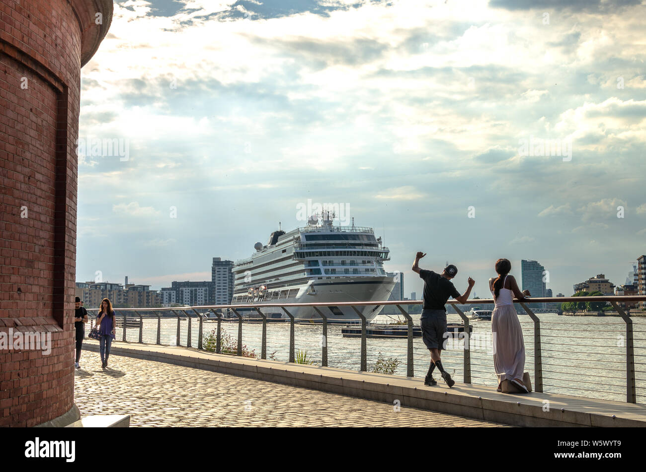 Tourists by the River Thames with MV Viking Sky cruise ship in the background at Greenwich, London Stock Photo