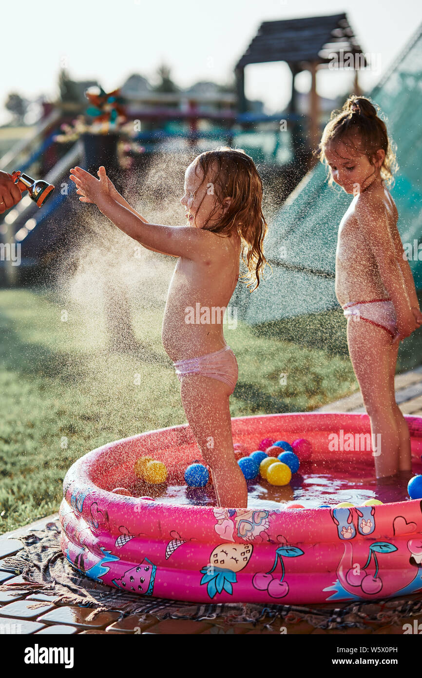 Little cute adorable girls enjoying a cool water sprayed by their father  during hot summer day in backyard. Candid people, real moments, authentic  sit Stock Photo - Alamy