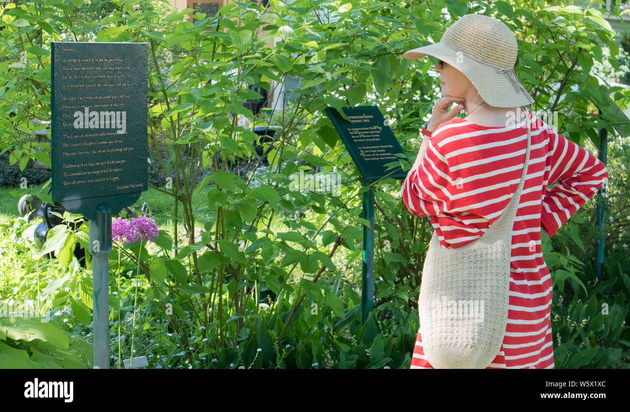Lady with large straw hat reading poetry of Mallarmé and Heine on plates planted in this beautiful bucolic garden. Niagara-On-The-Lake. Stock Photo